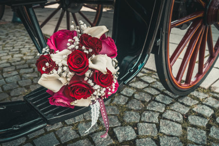Bridal bouquet with red, pink and white roses and white callas on the step of a black carriageの写真素材