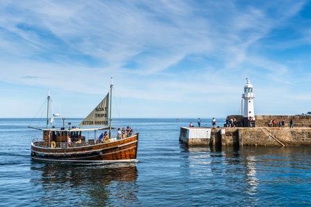 Mevagissey, Cornwall, UK - August 16, 2023: The lighthouse and harbor entrance at Mevagissey on the south coast of Cornwall. A tourist boat is coming back from a tour.のeditorial素材