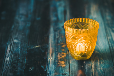 Yellow glass with tea light on blue wooden tableの写真素材