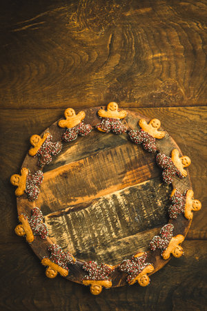 Sweet cookie characters with chocolate on the edge of a wooden plate on a dark wooden background, top view with copy spaceの写真素材