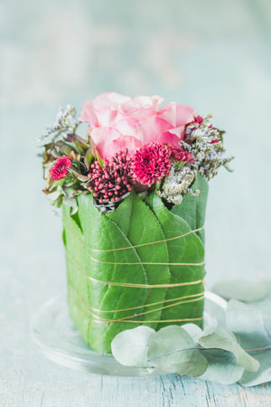 Small flower arrangement with rose as a gift or decoration, wrapped with green leaves on rustic wooden tableの写真素材