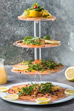Salmon carpaccio with lemon and rocket on a cake stand, Italian starter, antipasti, gray background, vertical.の写真素材