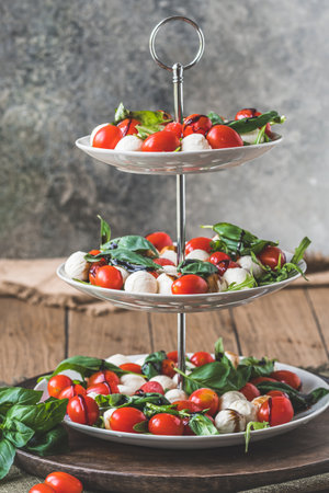 Classic Italian salad Insalata Caprese with cherry tomatoes, mini mozzarella pearls, basil leaves and balsamic glaze served on a cake stand, verticalの写真素材