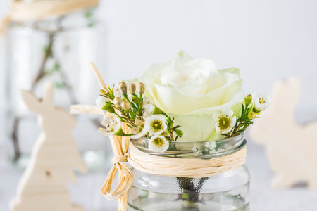 White rose in preserving jar, decorated with spring flowers, spring or easter decorationの写真素材