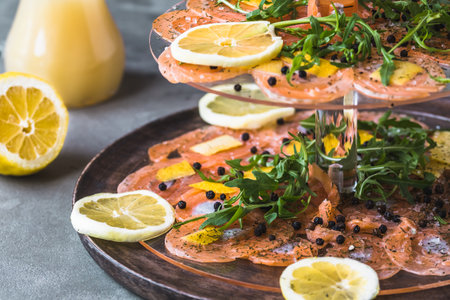 Salmon carpaccio with lemon and rocket on a cake stand, Italian starter, antipasti, gray background, vertical.の写真素材