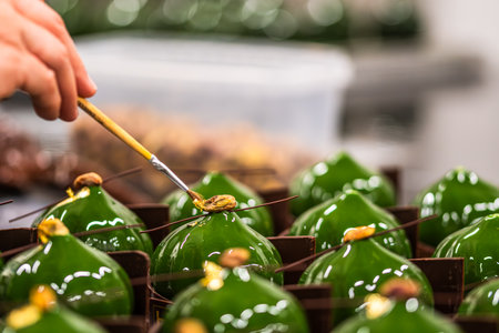 Hand of the confectioner decorating green glazed tarts with a brush with gold leaf. Preparation of the tarts by a professional pastry chef.の写真素材