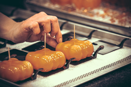 Hand of the female confectioner decorating orange glazed tarts. Preparation of the tartlets by a professional pastry chef.の写真素材