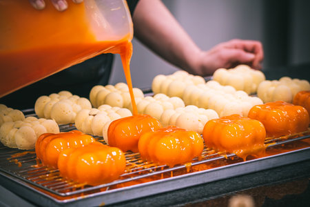 Confectioner's hand covering tartlets with an orange glaze. Preparation of the tartlets by a professional pastry chef.の写真素材