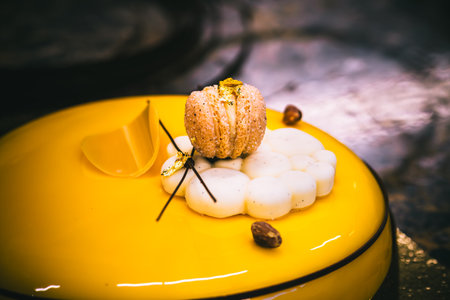 Tart with a yellow glaze, macaron, cookie, chocolate and gold decoration, dark background, close up.の写真素材
