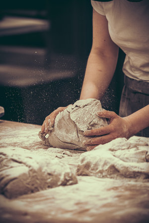 A female baker kneads bread dough in the bakery. Vintage style with grain. Verticals.の写真素材