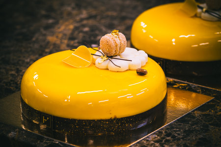 Tart with a yellow glaze, macaron, cookie, chocolate and gold decoration, dark backgroundの写真素材