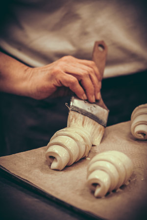 Hand brushes liquid butter or glaze onto raw croissants, vertical. Vintage style with grain.の写真素材
