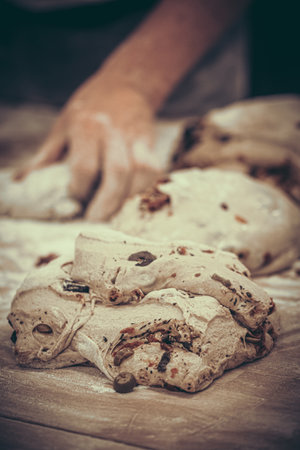 Raw bread dough with olives, tomatoes and herbs, on the wooden work table, prepared for further processing in a bakery, vintage style with grainの写真素材