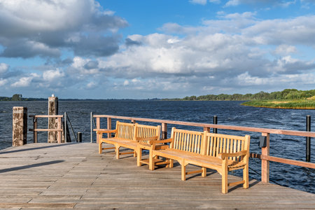 Two wooden benches on a wooden deck on a lake or riverbankの写真素材