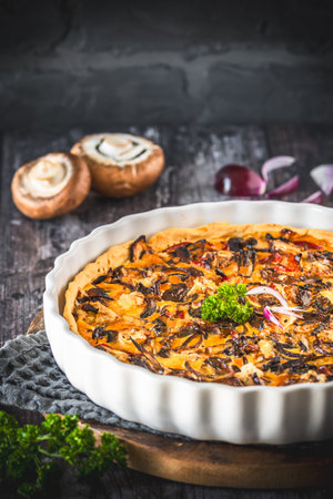 Whole tart, quiche with caramelized mushrooms, red onions and parsley on a dark background, vertical