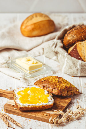 Half of a roll spread with cream cheese and lemon curd, variety of bread rolls in the background, scene of a breakfast, verticalの写真素材