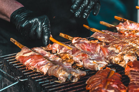 Hands with gloves turn Thai meat skewers on the grill, Asian street foodの写真素材
