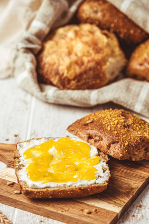 Half of a roll spread with cream cheese and lemon curd, variety of bread rolls in the background, scene of a breakfast, verticalの写真素材