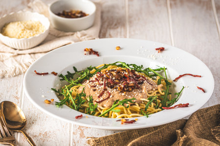 Spaghetti with chestnut sauce and crispy ham topping and arugula leaves on white wooden background, Italian foodの写真素材
