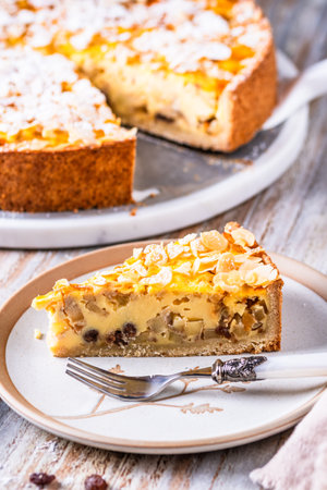 A piece of homemade apple pie with roasted almonds on white wooden background, whole cake in the background, verticalの写真素材