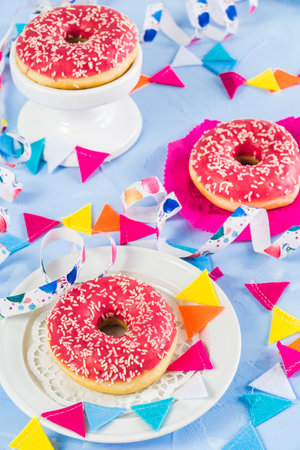 Pink glazed donuts on a light blue background, decorated with streamers and a party garland, verticalの写真素材