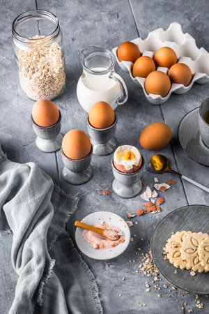Boiled brown eggs in gray egg cups and other breakfast ingredients on gray background, preparation for breakfast, verticalの写真素材