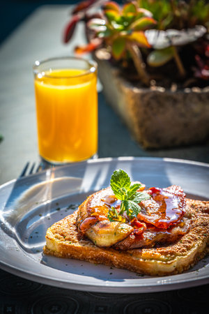 Breakfast in the sun with orange juice and French toast, bacon and fried banana, on green background, verticalの写真素材