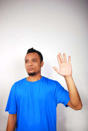 Young man with blue shirt raising hand in 'high five' or tentative wave, isolated background.の写真素材