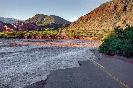 Mountain road cut by a rising river that eroded the land. Concept of immobilizing, blocking.の写真素材