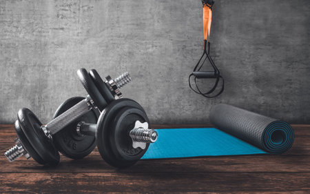 Dumbbells on wooden floor with yoga mat and  straps in the back.の写真素材