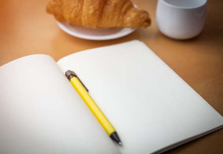 white notebook and yellow pen with croissant on wood table, business vintage conceptの写真素材