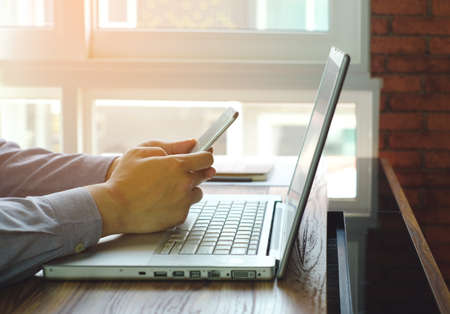 man playing mobile phone with laptop in office room
