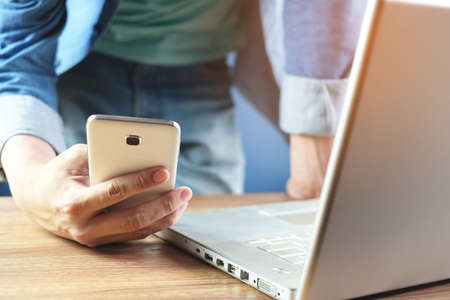 businessman working on mobile phone beside with laptop on wooden office table