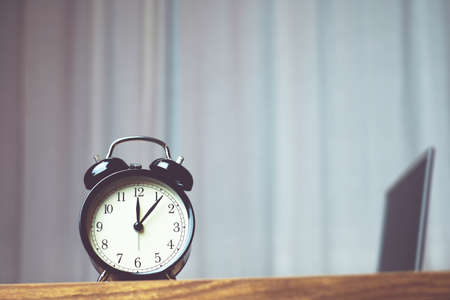 black bell clock on the wood table with computer laptop background