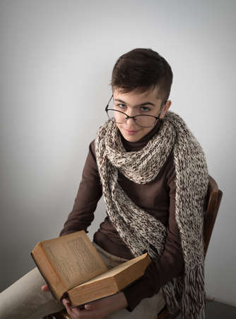 Lutsk. Ukraine. February 1, 2020; Young stylish student man is reading an old book, sitting on an old wooden chair on a white background.のeditorial素材
