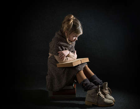 Lutsk. Ukraine. February 1, 2020; A girl wrapped in a warm brown shawl sits on a stack of old books and reads the yellowed pages.のeditorial素材
