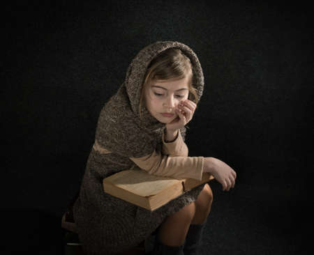 Lutsk. Ukraine. February 1, 2020; A girl wrapped in a warm brown shawl sits on a stack of old books and reads the yellowed pages.のeditorial素材