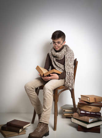 Lutsk. Ukraine. February 1, 2020; Young stylish student man is reading an old book, sitting on an old wooden chair on a white background.のeditorial素材