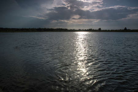 Solar path on the water. Skyline silhouette. Reflexes on the waves. Dark evening clouds of sunset. The lights of a sun.の写真素材