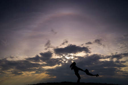 Lutsk. Ukraine. May 1, 2020; A young mother twists a child around her. Silhouette against a dark...