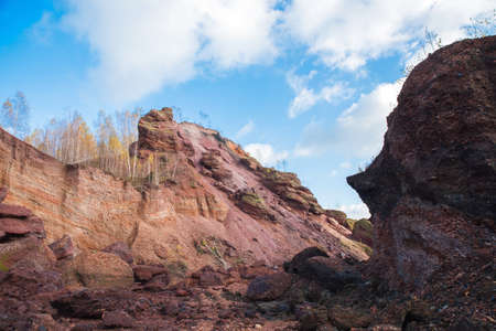 Red mountains with autumn trees and blue cloudy sky. Colored waste heaps after extracting coal from...