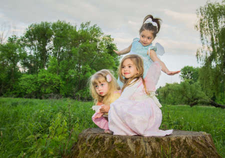 Little cute girls with butterfly wings on a large tree stump among the tall green grass. Selective...
