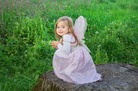 Little cute girls with butterfly wings on a large tree stump among the tall green grass. Selective...