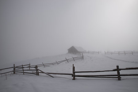 Old wooden barn high in the mountains in winter in the clouds. Thick fog. Selective focus. Blurred background.の写真素材