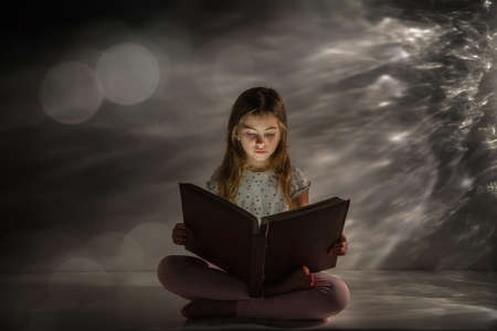 The girl is reading a book of fairy tales. Dream. Mystery. Fantasy. Spectacular background. Light glare.の写真素材
