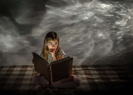 The girl is reading a book of fairy tales. Dream. Mystery. Fantasy. Spectacular background. Light glare.の写真素材