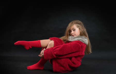 Teenage girl in a red fur coat in the studio on a black background.の写真素材