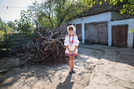 Odessa, Ukraine. August 25, 2017; A girl in national Ukrainian clothes, in a wreath on her head with red beads against a blue window near a rural house.のeditorial素材