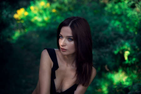 Beautiful brunette girl with blue eyes in the forest. Witching look. Sun spots and glare. Effective bokeh. Selective focus. Blurred background.の写真素材