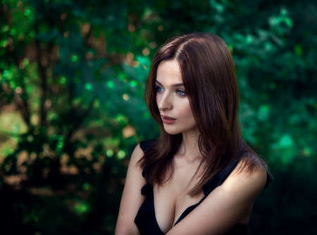 Beautiful brunette girl with blue eyes in the forest. Witching look. Sun spots and glare. Effective bokeh. Selective focus. Blurred background.の写真素材